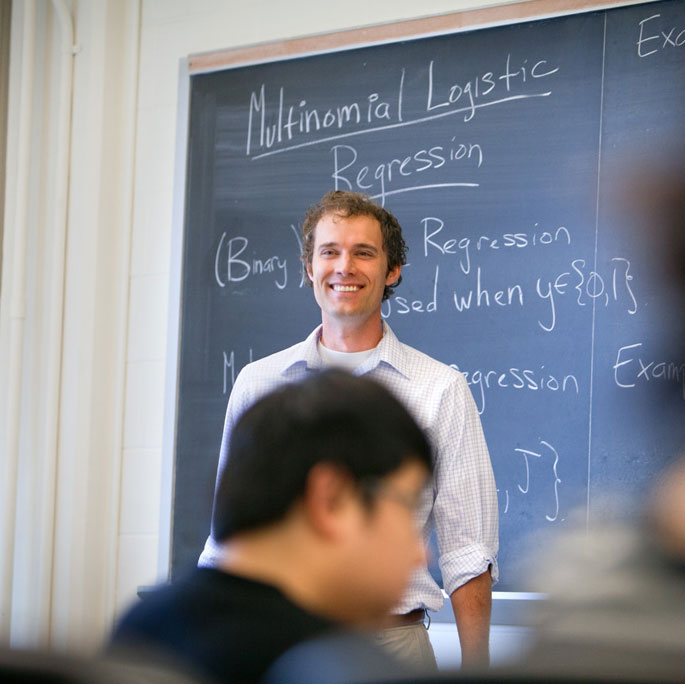 professor standing in front of chalkboard and teaching class