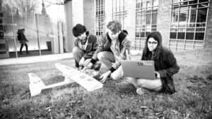 three students on campus lawn with project plane